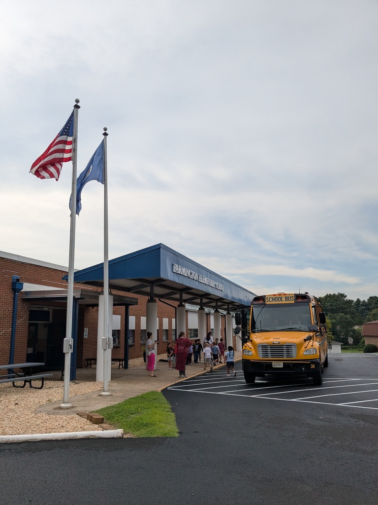 A school building with two flags, a yellow school bus, and children walking under an awning.