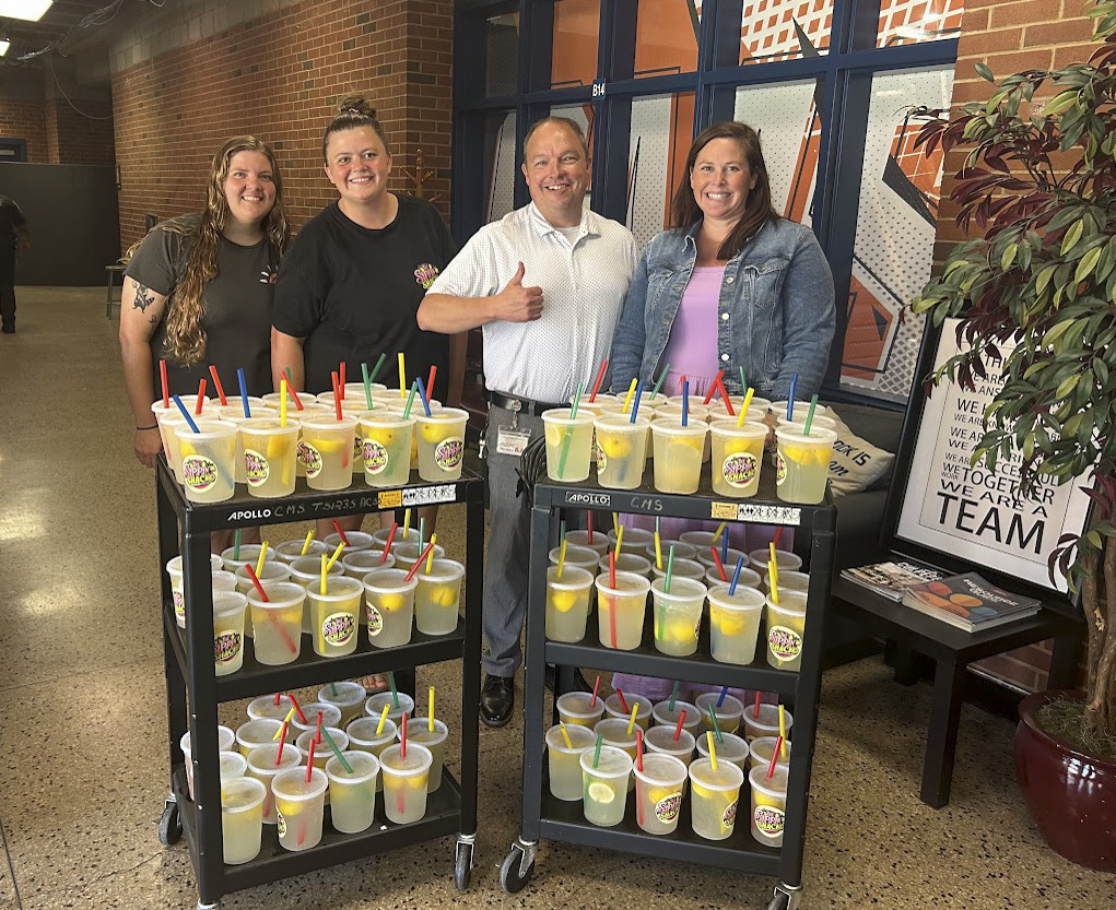 Four people smile behind two rolling carts filled with cups of fresh lemonade with colorful straws at Culpeper Middle School. The lemonade, provided by Sippin Shack, was donated by the CTEC National Honor Society as a special treat for CMS teachers and staff.