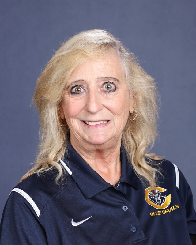 Woman with blonde hair, wearing a blue polo shirt with a Nike logo and a logo reading "Blue Devils".