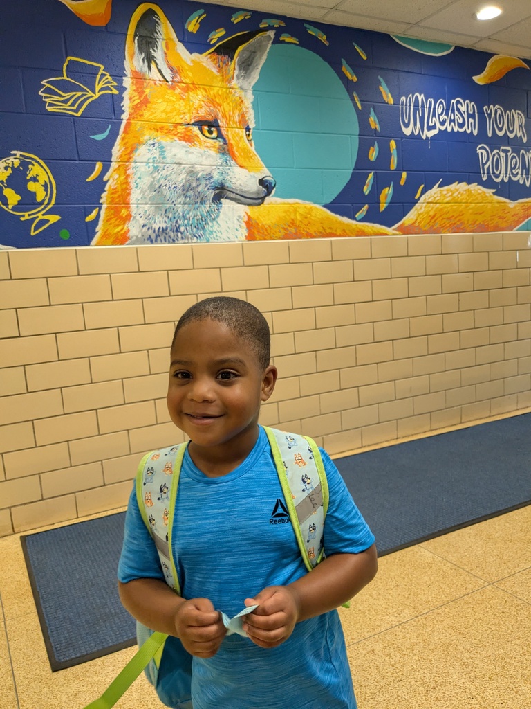 A child in a blue shirt and backpack stands in a hallway with a red fox mural behind them.