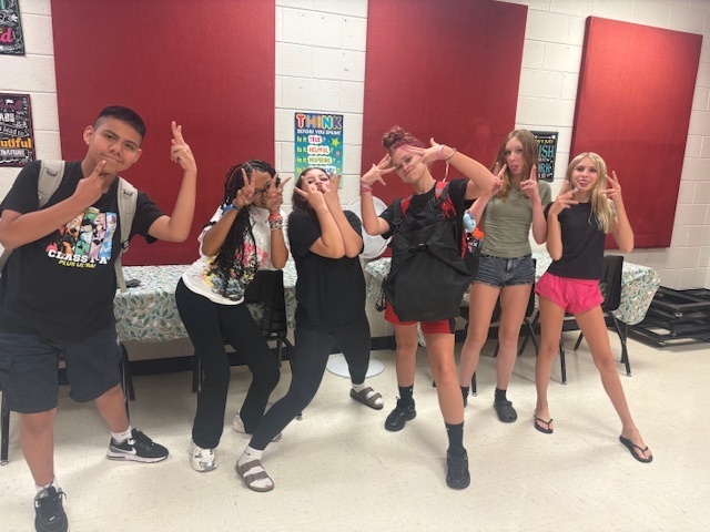 A group of young people standing in a room with red walls, smiling and posing for a photo.