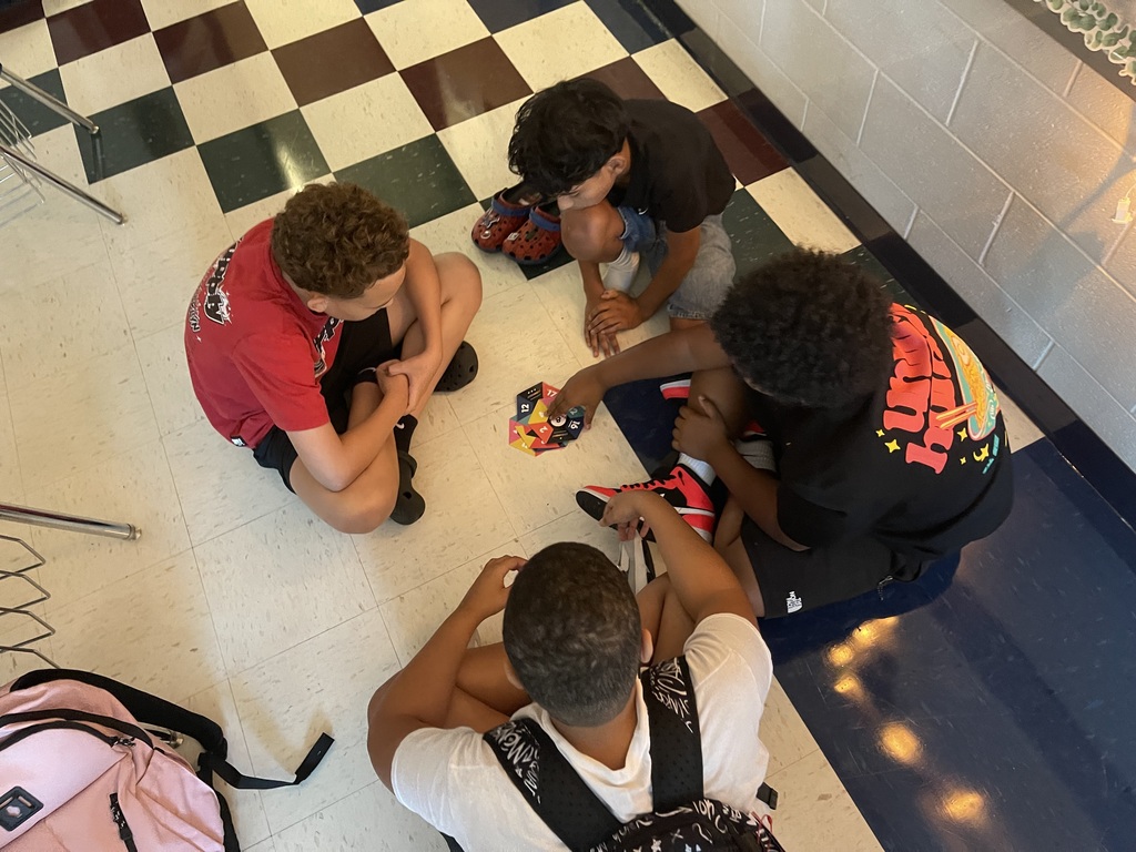 Four people on a checkered floor, working on shoes. Two have backpacks; one is pink.
