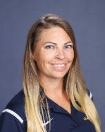 Woman with long blonde hair smiling, wearing a navy blue polo shirt with white trim and a logo.