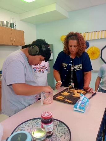 Three people work at a kitchen counter with cookies, with one person wearing headphones.