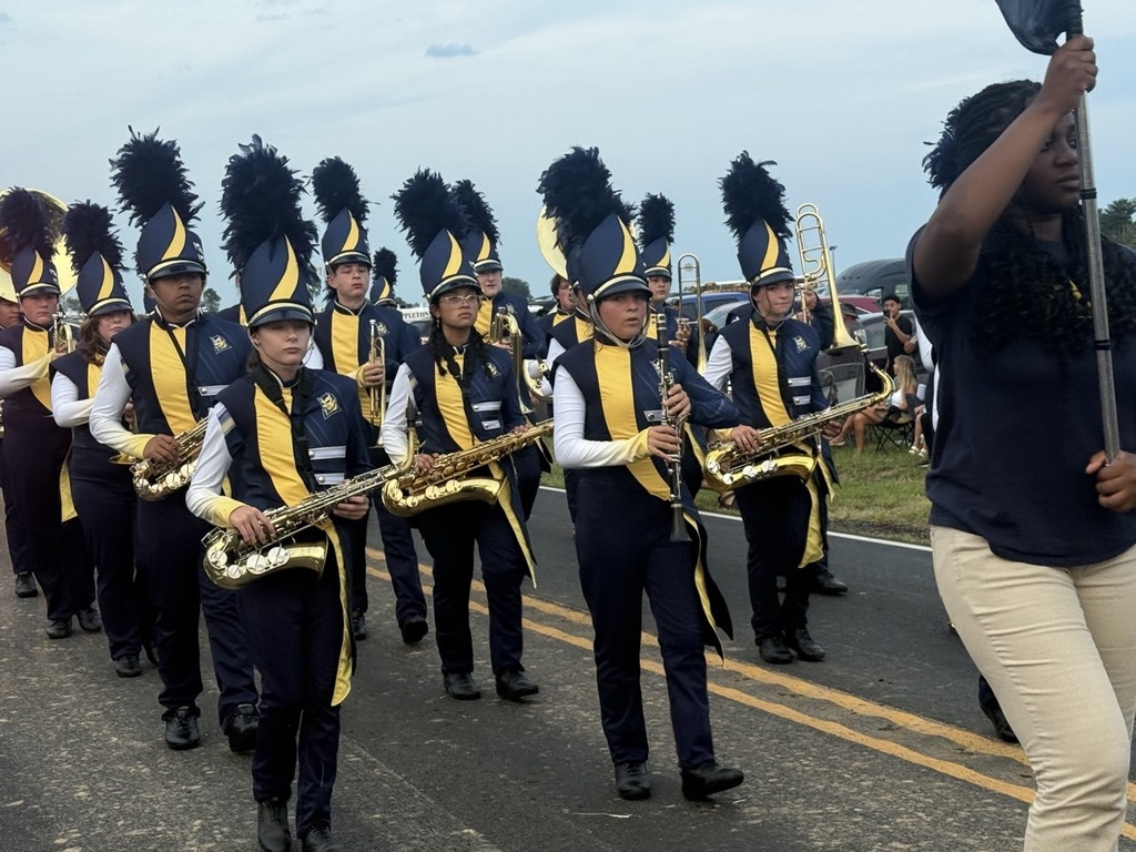 A marching band of students in blue, yellow, and black uniforms playing saxophones and trumpets in a parade.