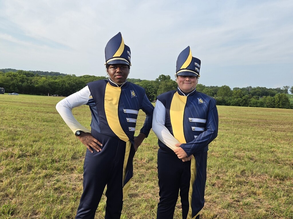 Two people in blue, white, and yellow uniforms with hats standing in a field with green grass.