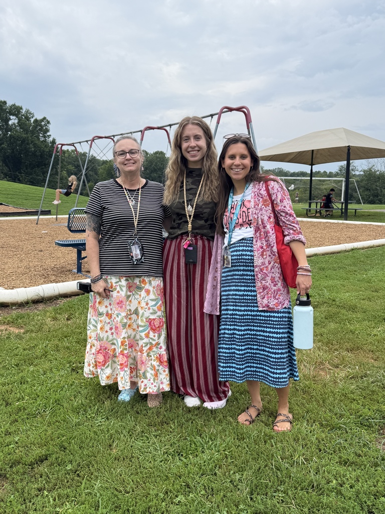 Three school staff members smile together outdoors near the playground.