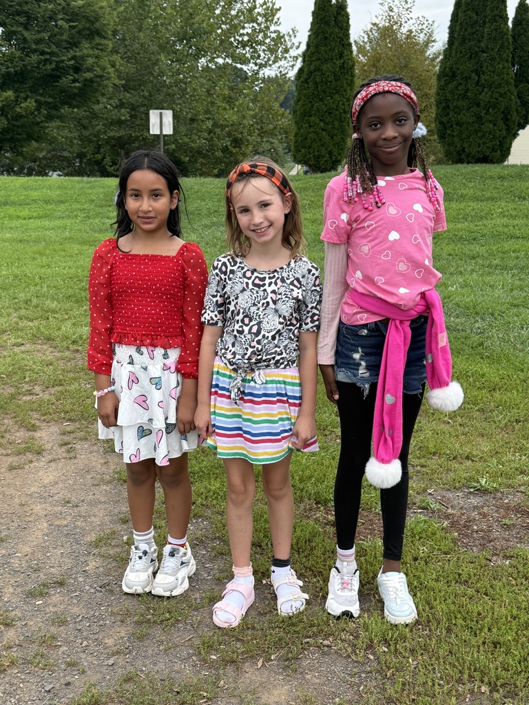 Three elementary students pose together outdoors on a grassy area during a school activity