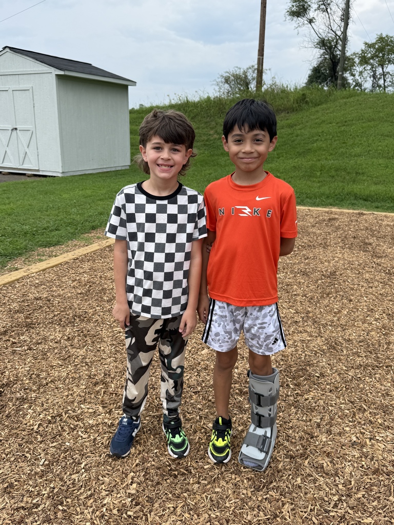 Two elementary students smile together on a wood-chip playground area.