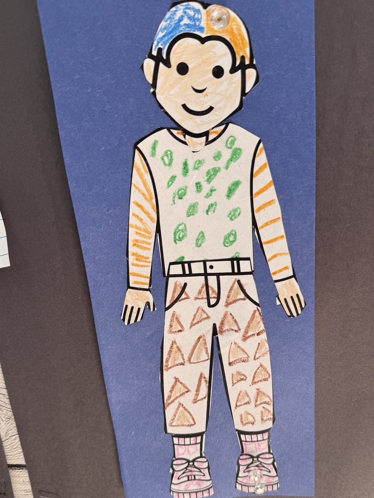 A student-created paper figure decorated with colorful patterns is displayed on blue construction paper.
