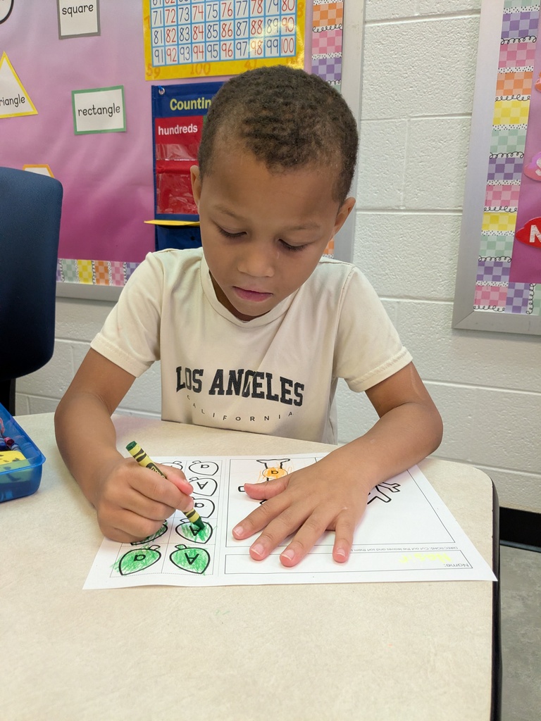 Student is coloring a worksheet with a green crayon about uppercase A and lowercase a.