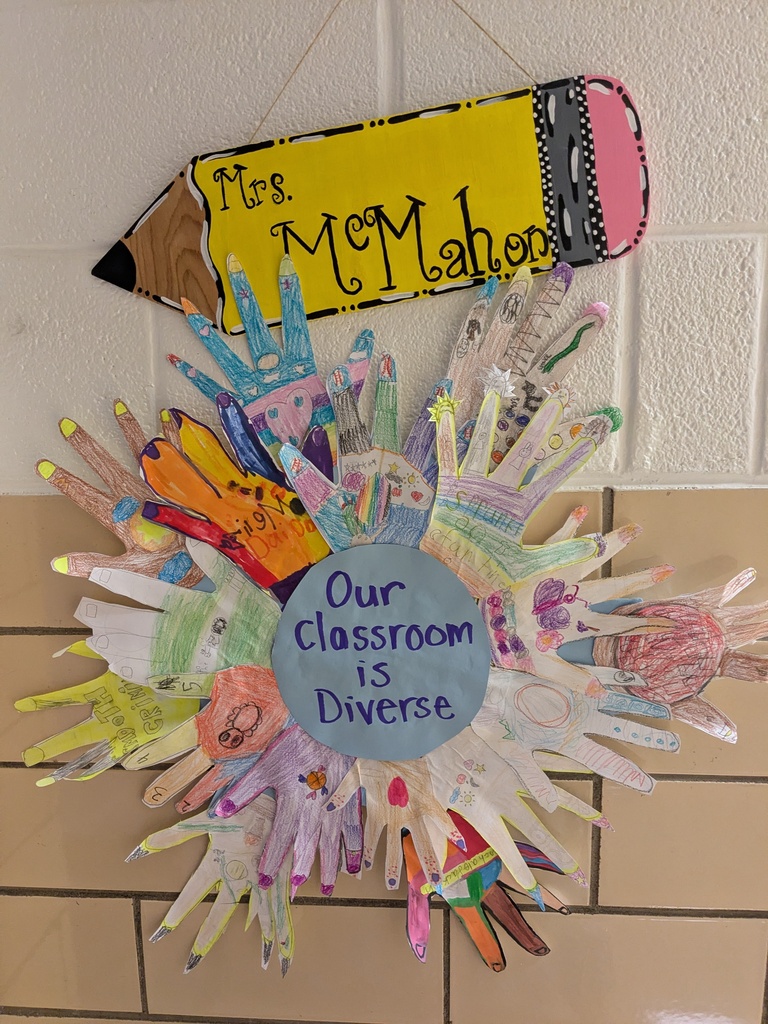 A colorful wreath of children's hands hangs on a white wall. Above it, a pencil sign reads "Mrs. McMahon."