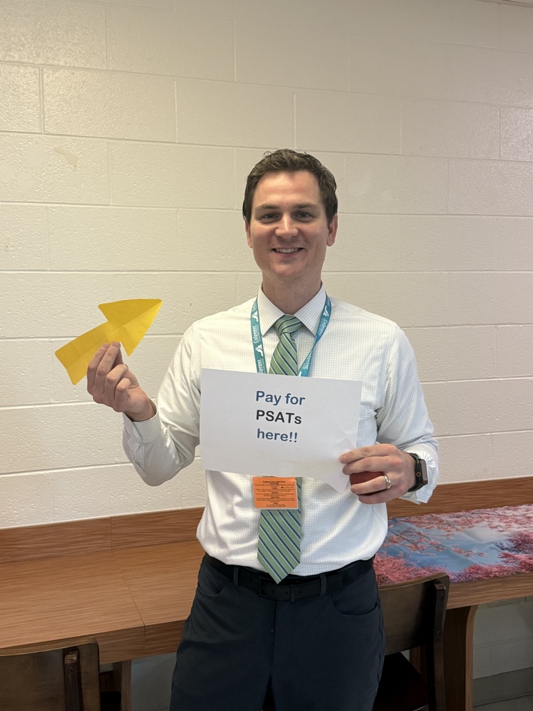 A man in a white shirt and tie holds a sign reading "Pay for PSATs here!" and a yellow paper.