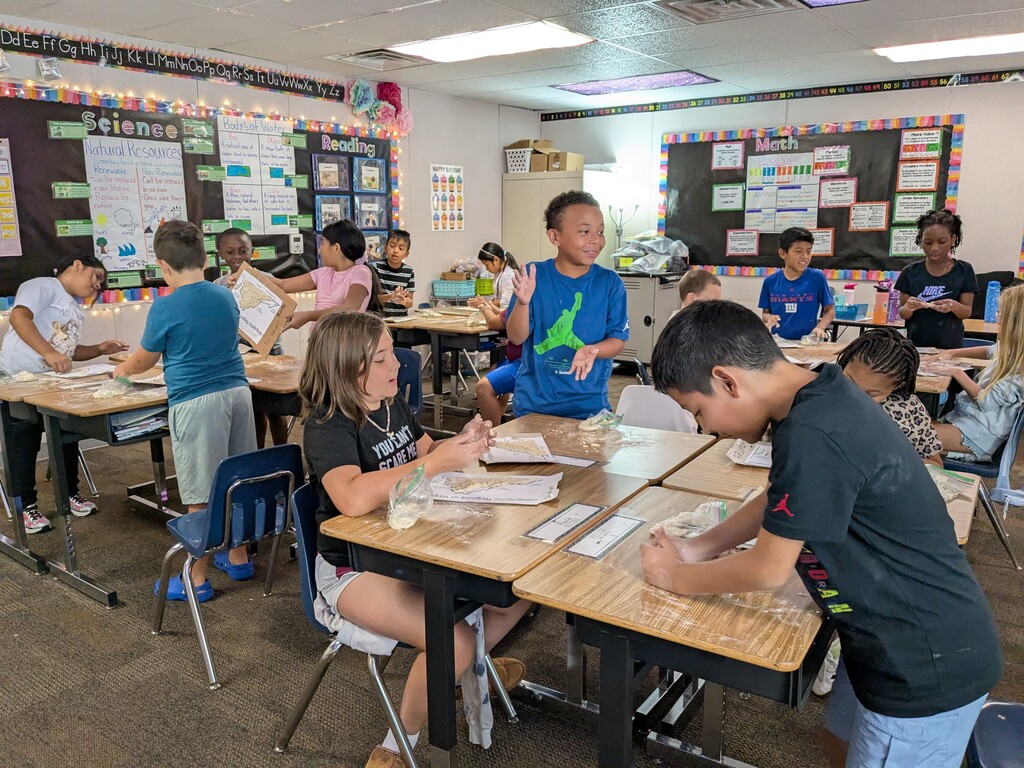 A classroom with children seated at desks, engaged in a group activity with materials on the table.