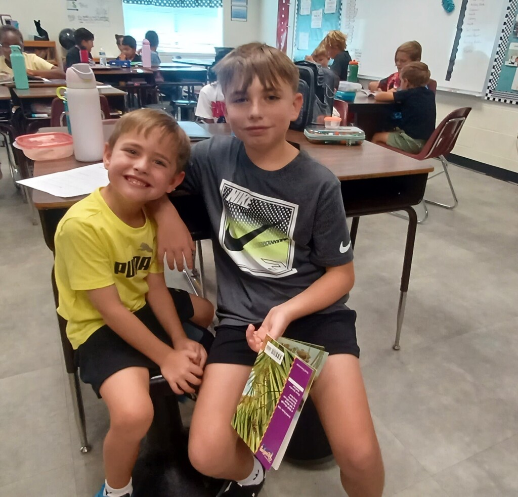Two boys seated in a classroom, one with a yellow shirt and the other in gray.