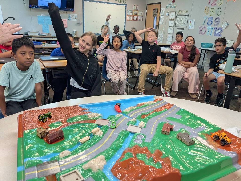 Classroom with children sitting around a table. A large model of a town is on the table.