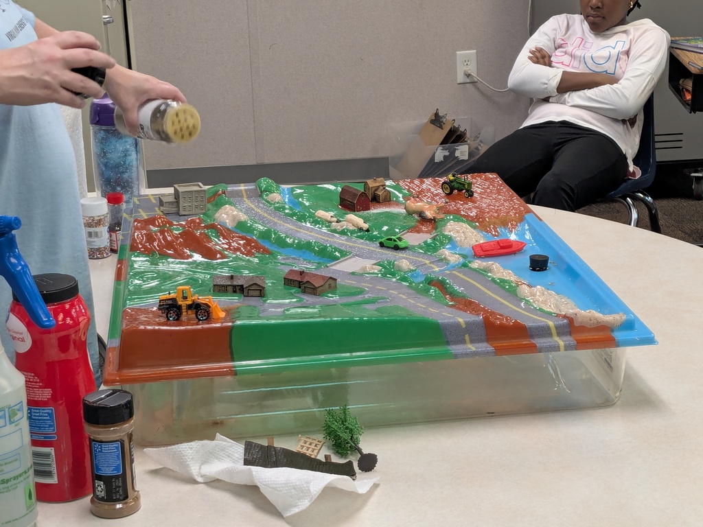 A model of a road is displayed on a table. It has various structures, a roadway, and figures.