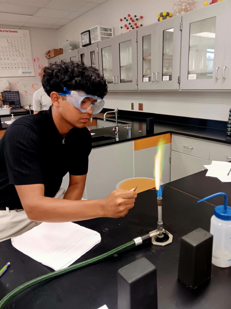 A person in a black shirt conducts a lab experiment in a lab, holding a lit Bunsen burner.