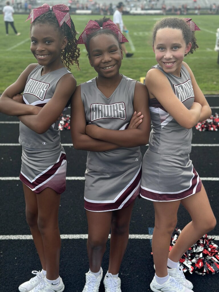 Three girls in cheerleading uniforms with maroon and gray accents smile for a photo on a track.