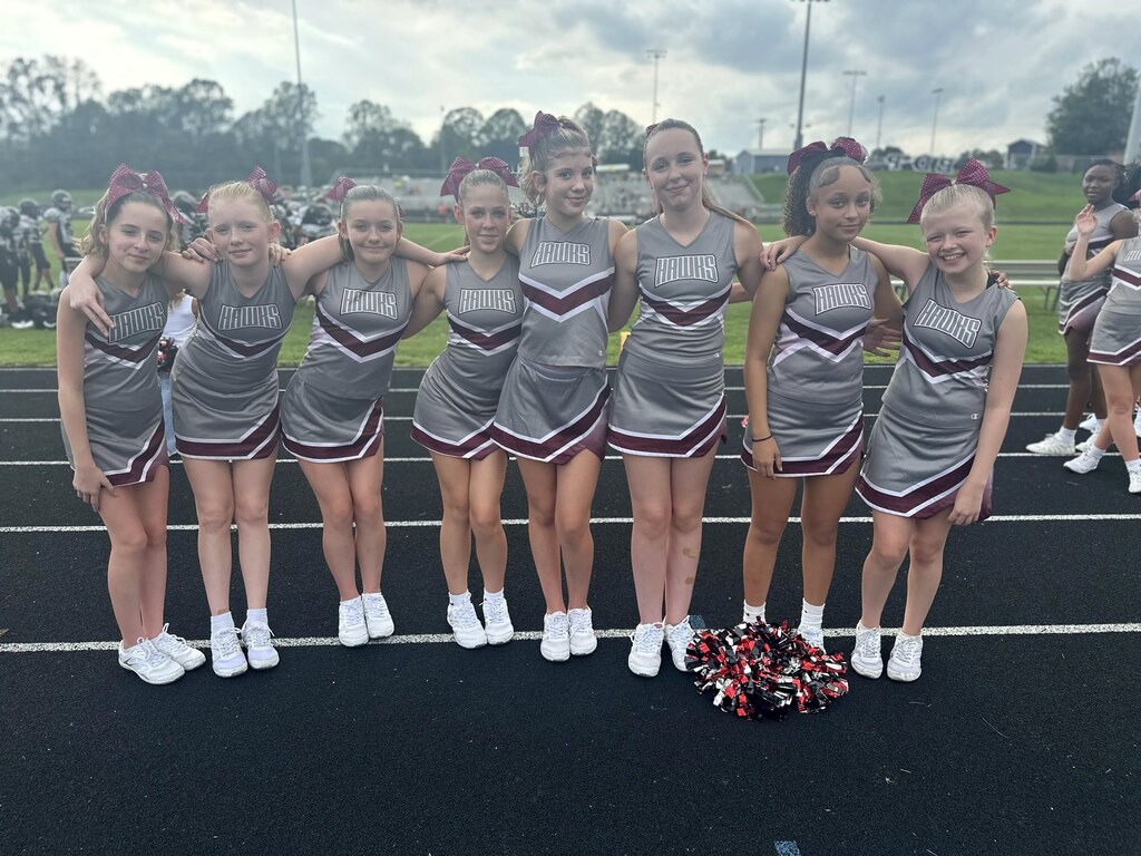 Six cheerleaders pose together on a track with pom-poms. They wear matching uniforms with maroon and gray stripes.