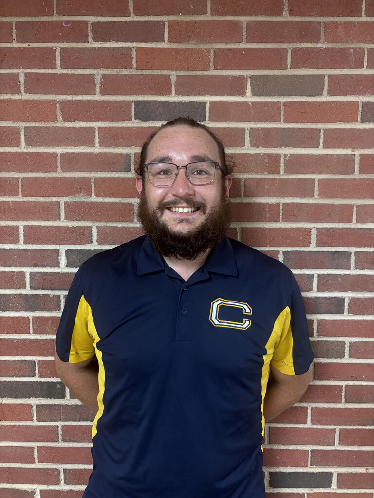 A man with a beard and glasses poses for a photo in front of a red brick wall.