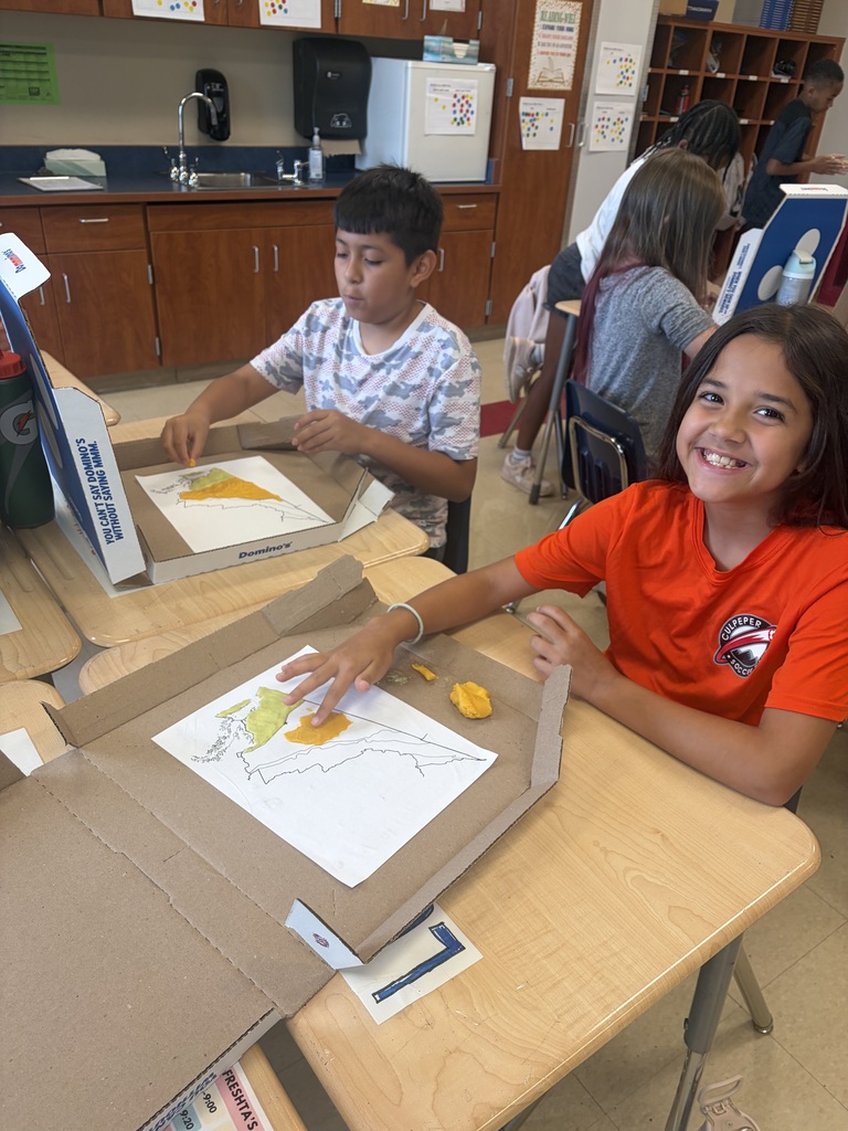 Students work at classroom desks using modeling clay and paper maps to create 3D representations of Virginia’s geographic regions.