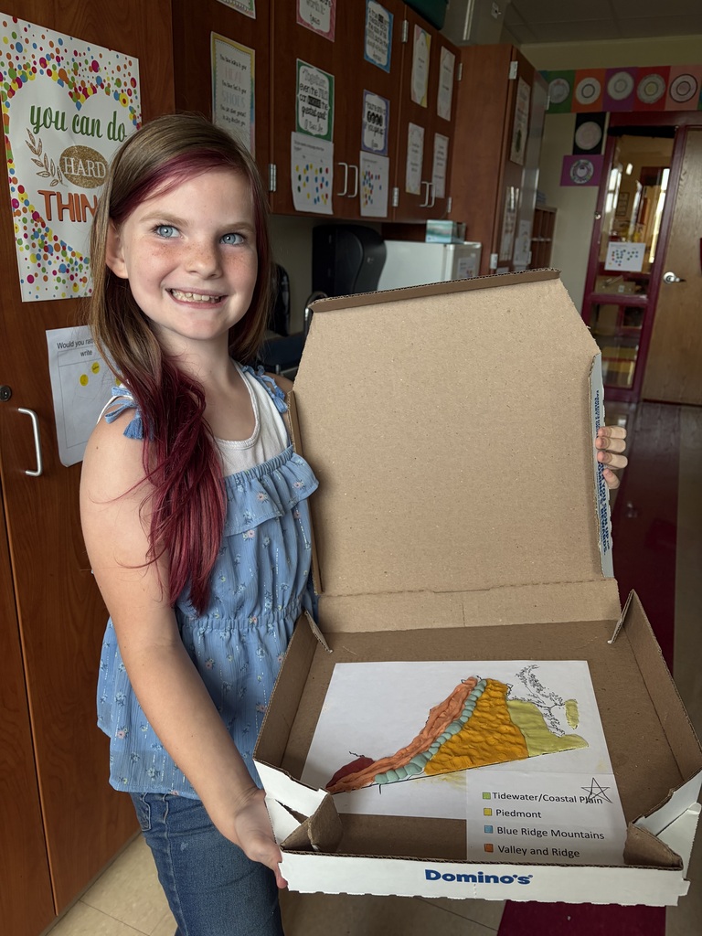 A smiling student holds an open pizza box containing her completed colorful 3D clay map of Virginia’s geographic regions.
