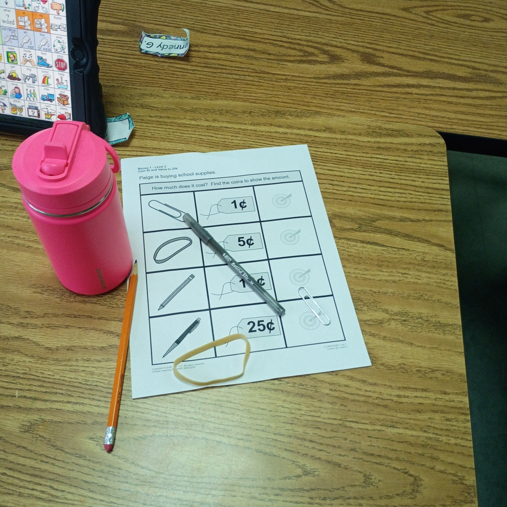 Table with a pink tumbler, pencil, rubber band, and a sheet of paper with lines and numbers.