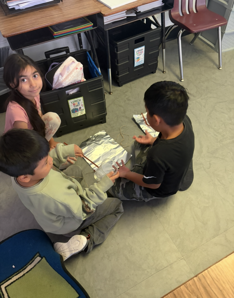 Three students seated on a floor, engaged in a hands-on activity with materials.