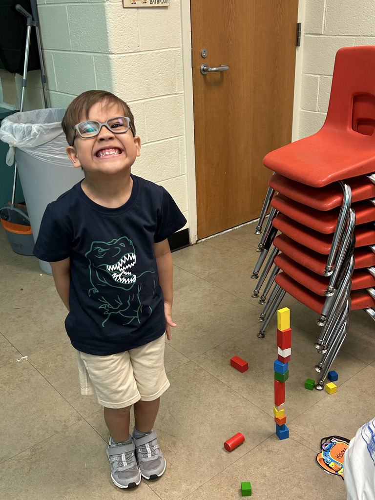 A child wearing glasses smiles while standing next to a stack of colorful blocks on a tiled floor.