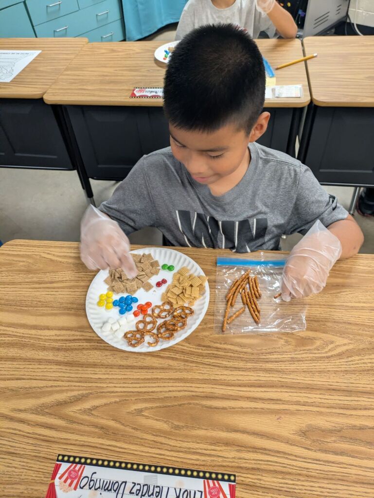 Child sitting at a table with a plate of colorful candies and pretzels in a classroom.