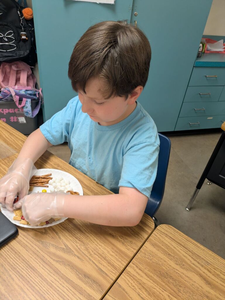 A boy wearing blue gloves is seated at a table, arranging food on a plate.