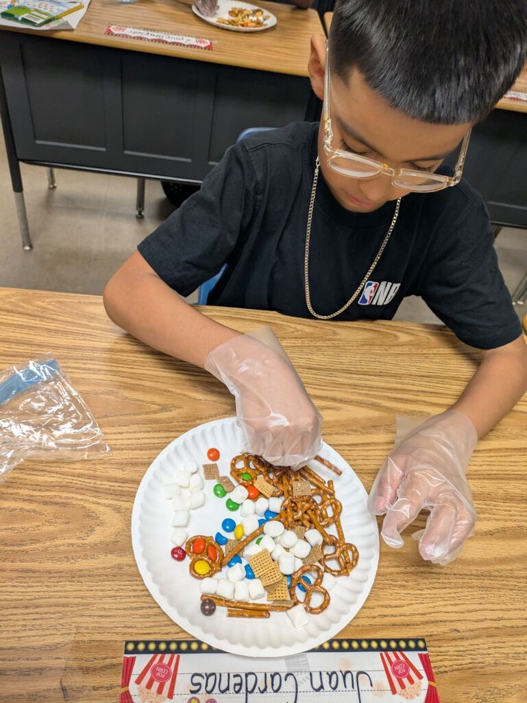 A young boy with glasses and gloves arranges a mix of candies and pretzels on a white plate.