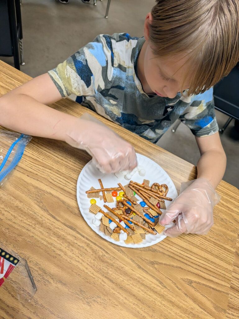 Child with gloves on, placing snacks on a paper plate to create a small structure.
