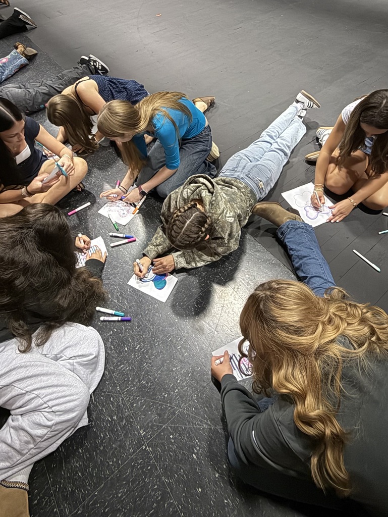 A group of people sitting on a floor, drawing with markers. Papers with drawings and markers on floor.