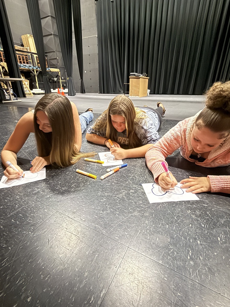 3 female students coloring butterflies while lying on the floor