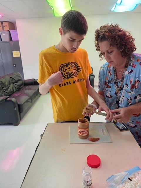 A person in yellow works with a woman in blue to open a jar of peanut butter.