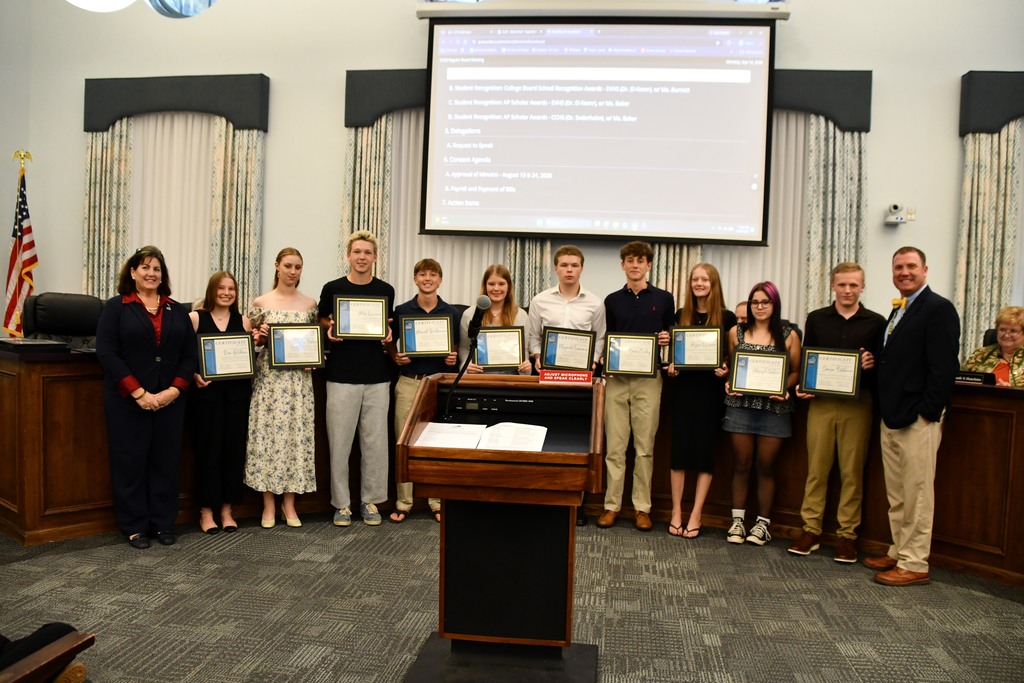 Group of individuals stand in a room with certificates. A podium and projector screen behind them.