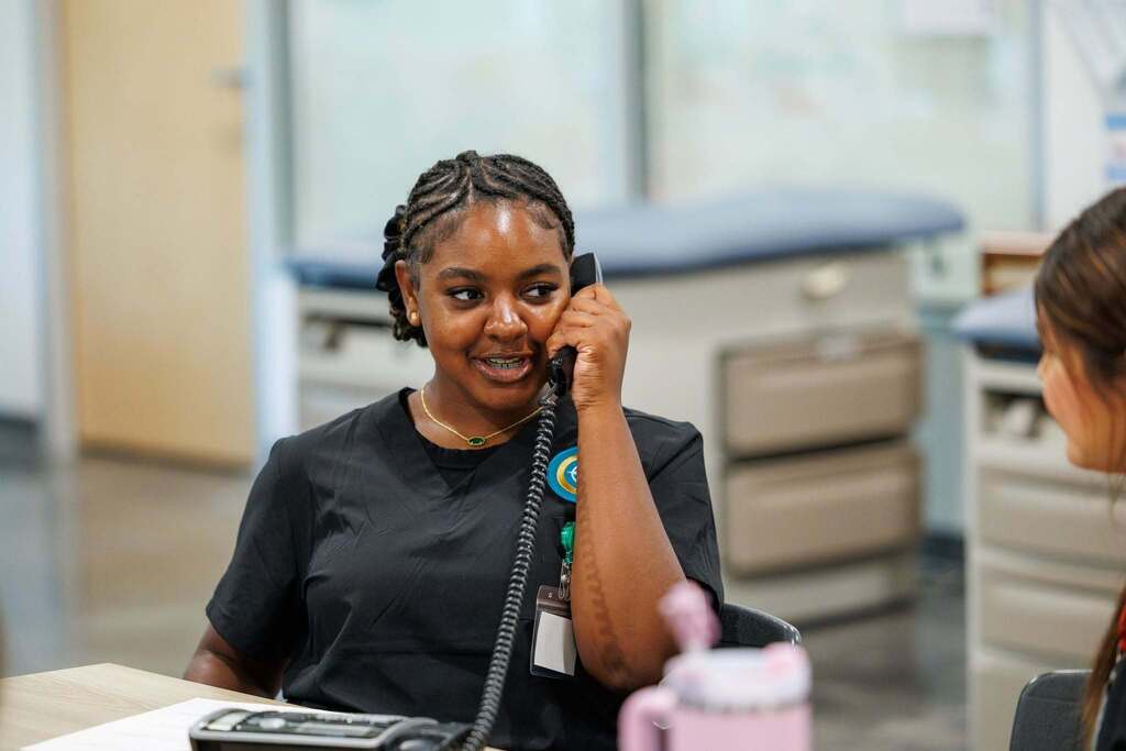 A CTEC Medical Assistant student practices professional telephone etiquette while speaking on a classroom phone during a hands-on communication activity.