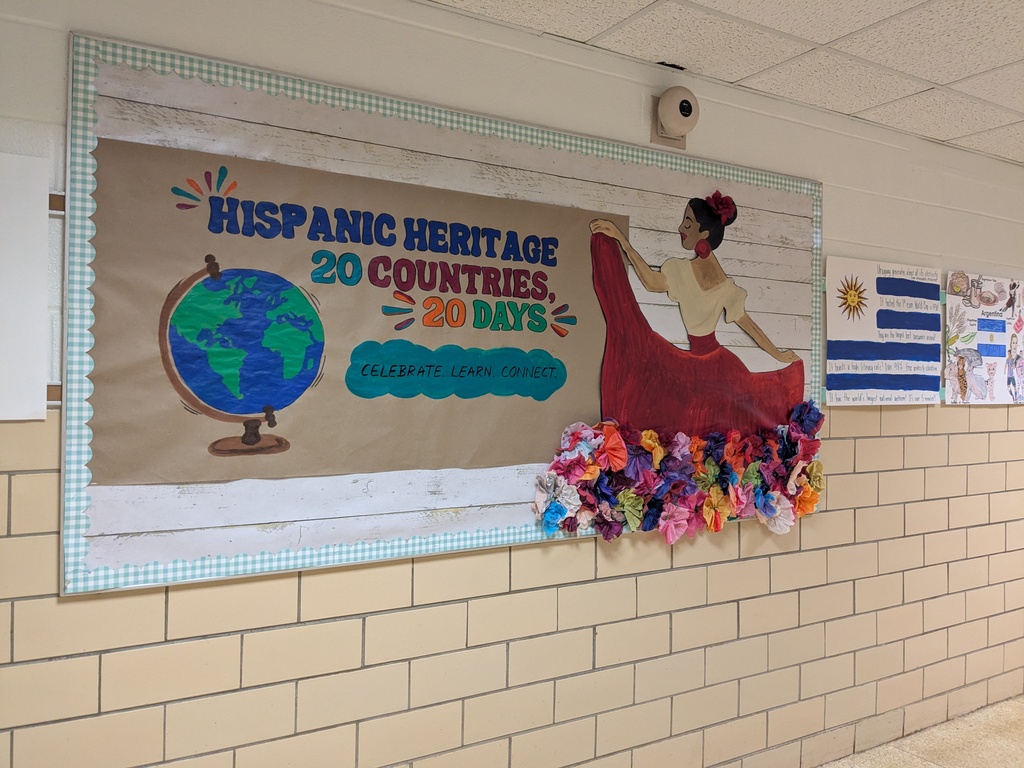 A hallway displays a bulletin board with Hispanic Heritage celebration details. It includes a globe, a woman, and a colorful garland.