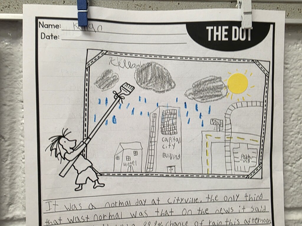 A classroom bulletin board with a student's drawing of a character holding a broom. The text reads "The Dot."