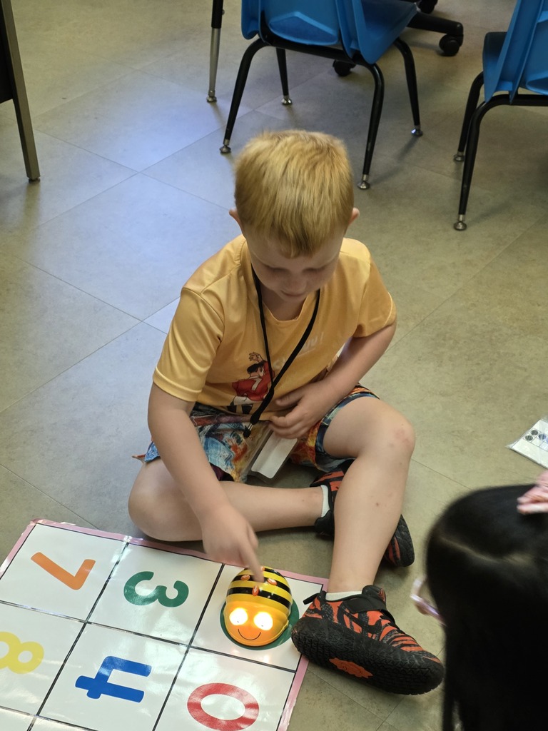 A child is seated on the floor, holding a toy, and playing a game with letters and numbers.