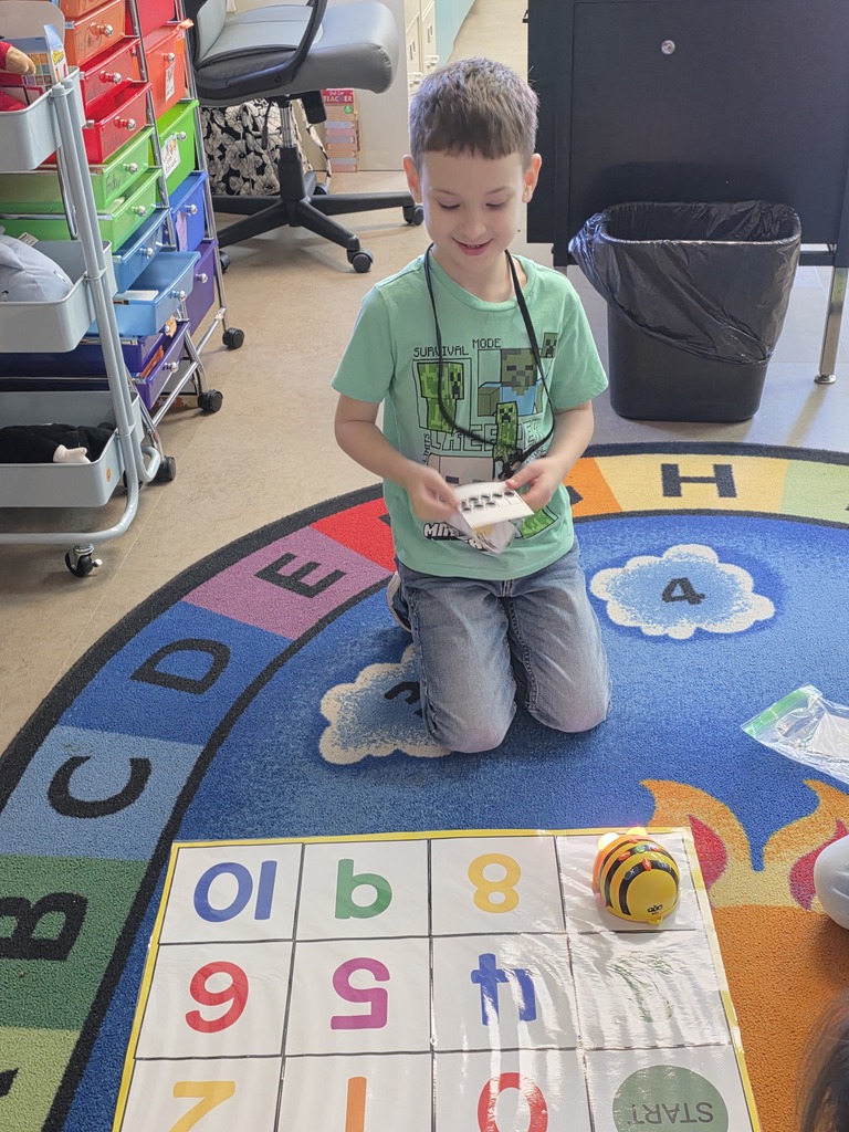 Child kneeling on a rug, holding a game piece and looking at an educational game board.