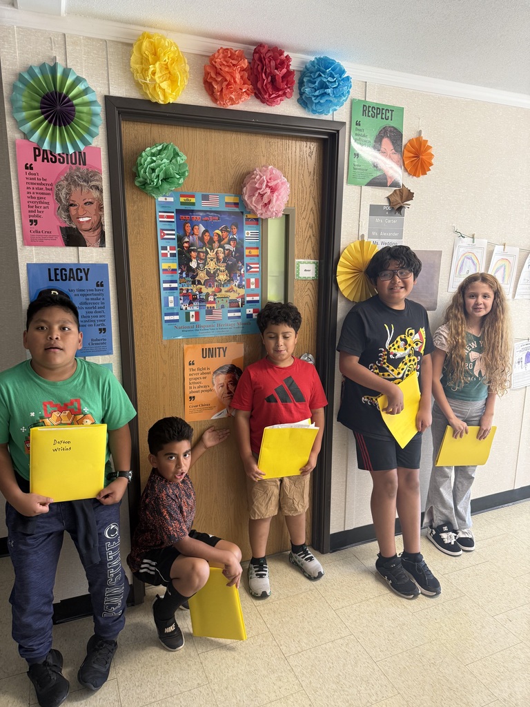Five children stand in a row, holding yellow folders, in front of a door with colorful decorations.