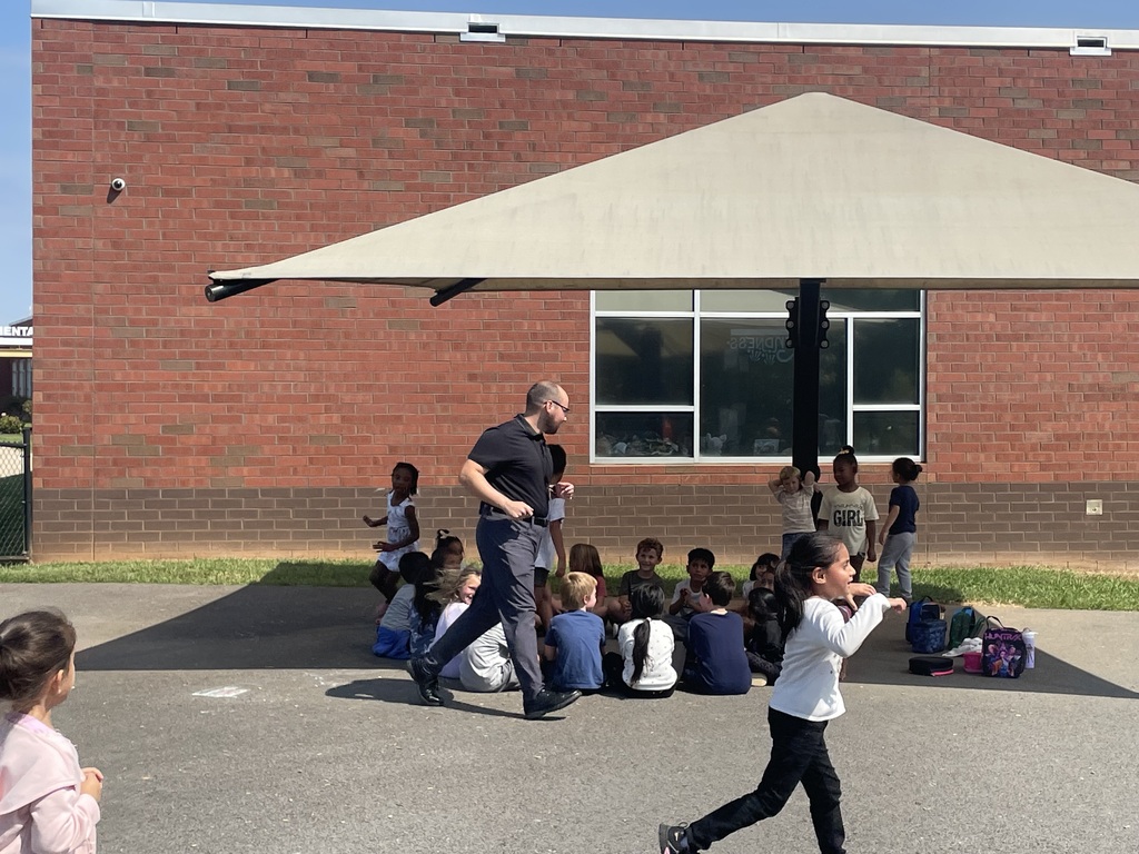 Adults and children outside in a courtyard under a canopy. One adult runs and one child runs.