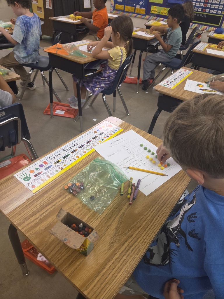 A classroom with children seated at desks, working on crafts. Each desk has papers and art supplies.