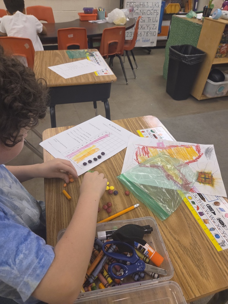 A child works at a desk with art materials, papers, and scissors. Another child sits in a chair.