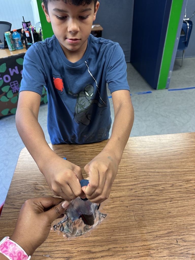A young boy in a blue shirt examines a clear plastic bag with a small object.
