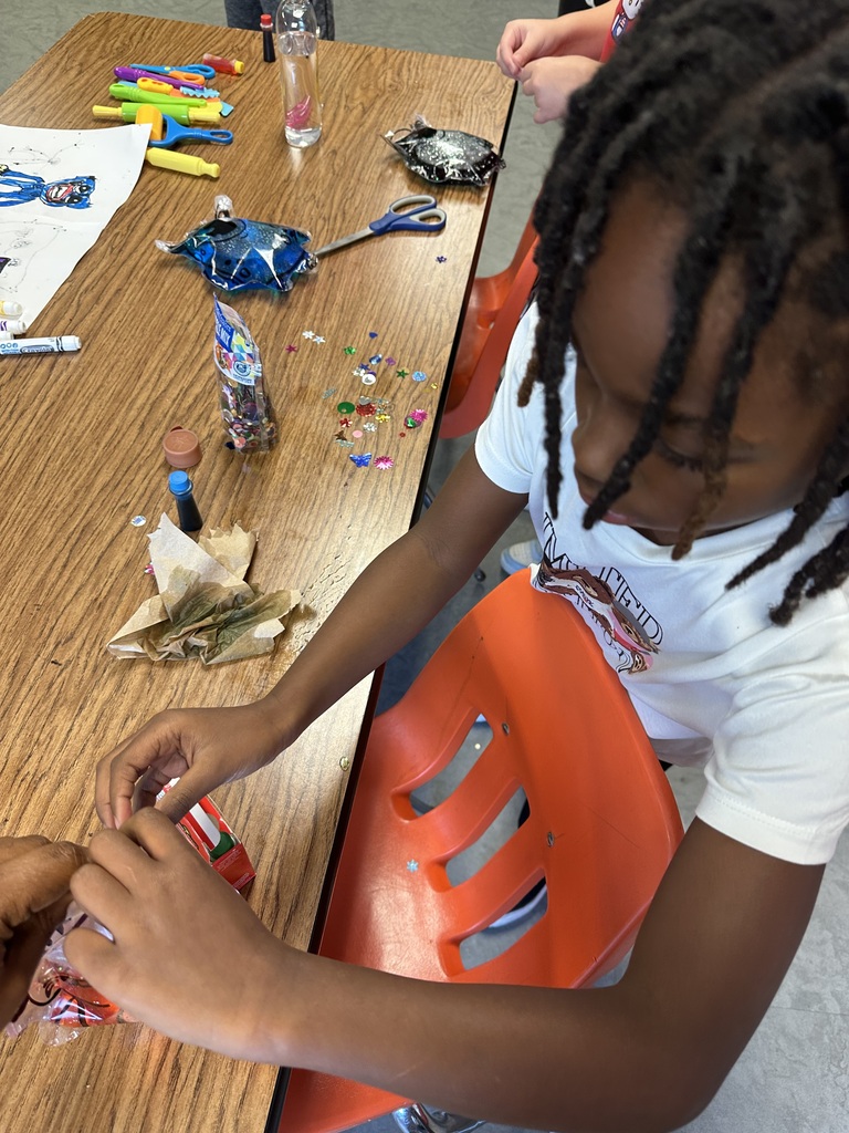 A child is seated, working on a craft project with various materials on a wooden table.