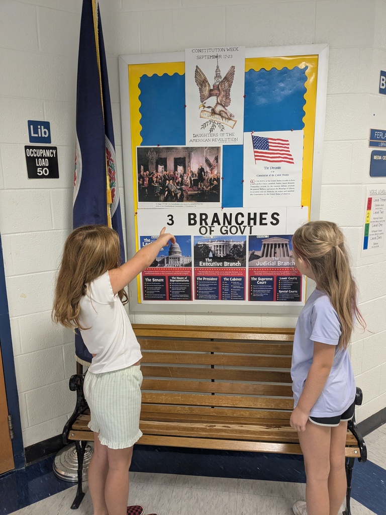 Two young girls stand next to a bulletin board about the 3 branches of government.